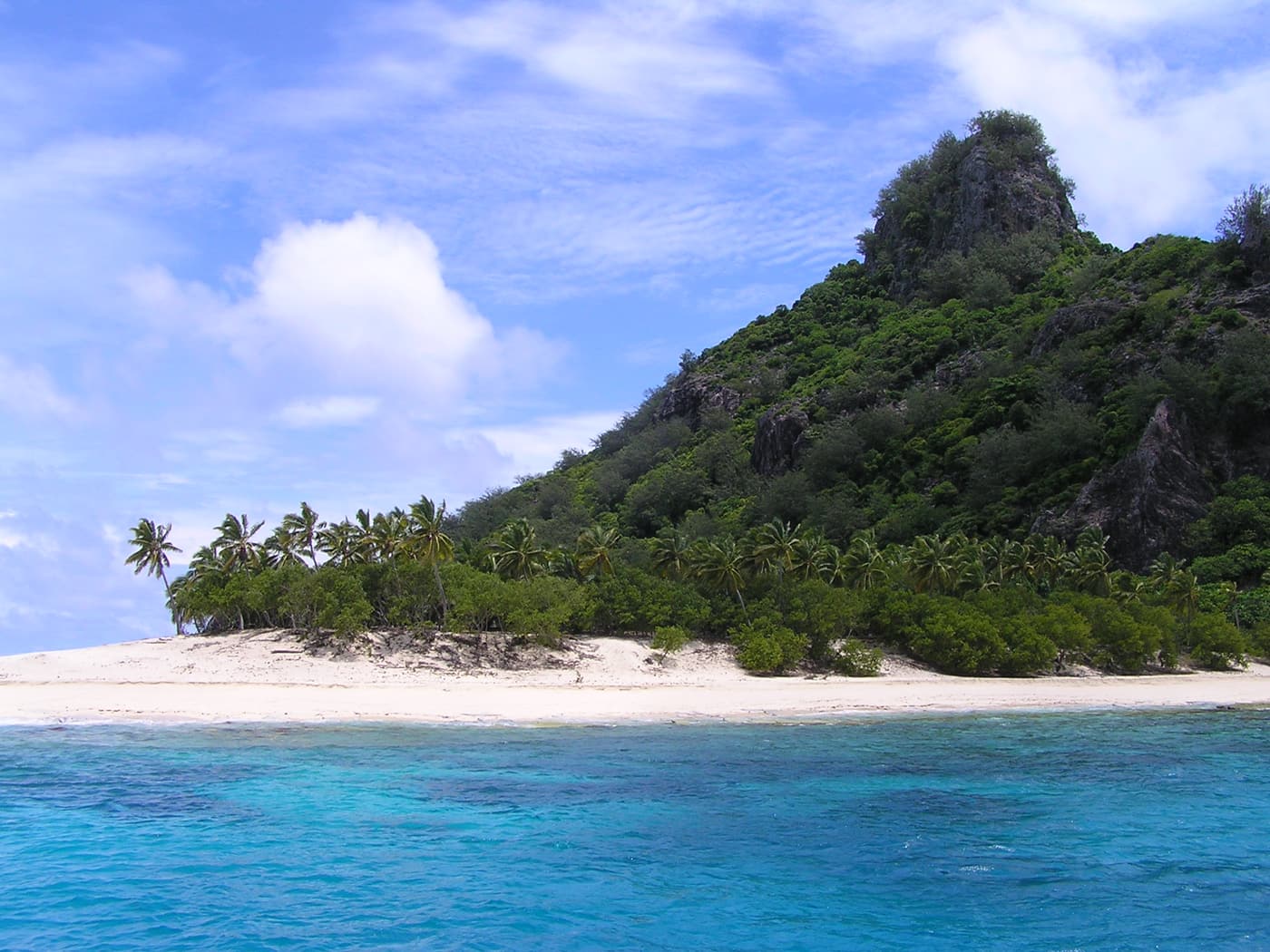 White sand and turquoise shallows below the jungle-clad peak of Monuriki