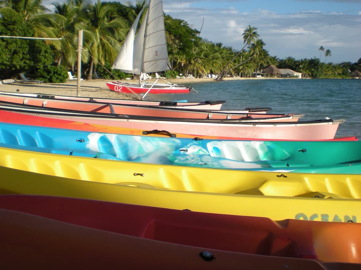 Colourful kayaks on the beach at Musket Cove with a sailing dinghy offshore